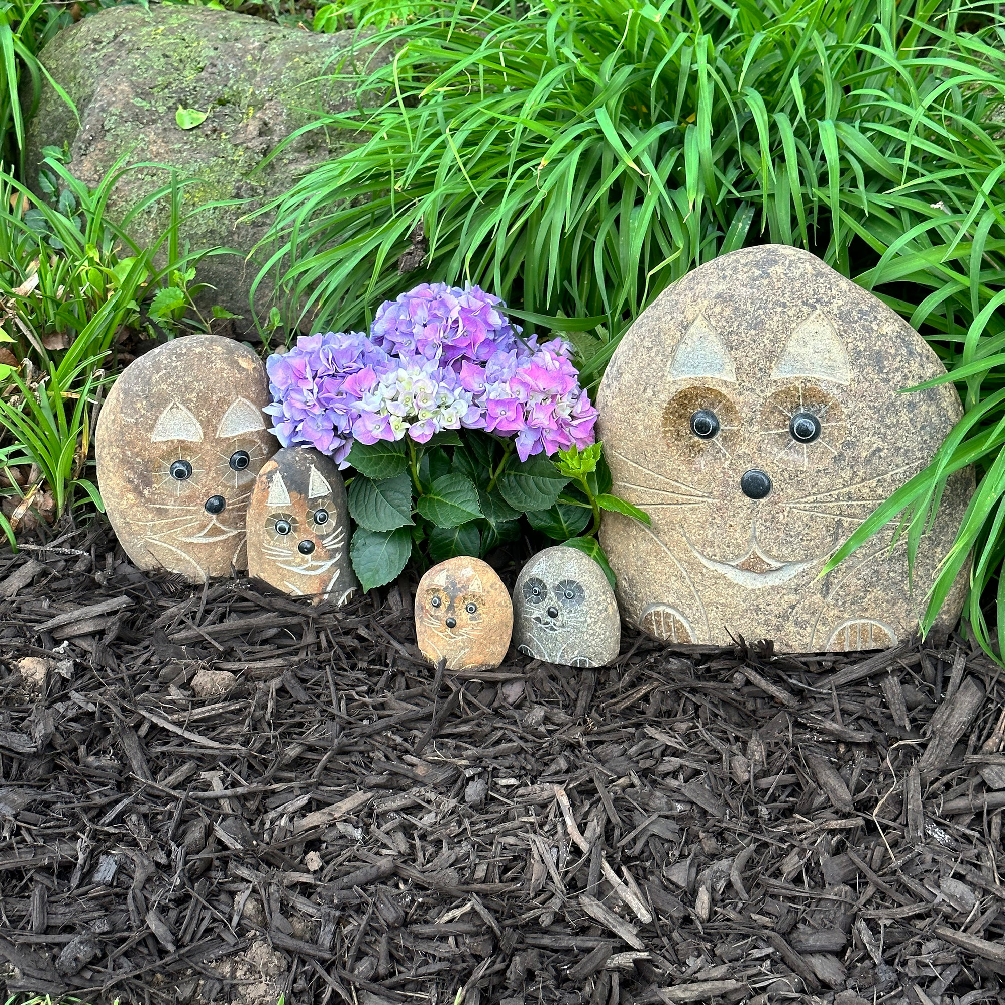 Hand-carved granite boulder stone cat family set of five in a garden setting.