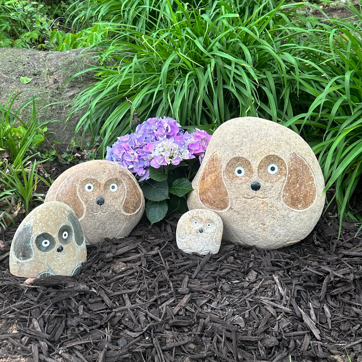 Hand-carved natural granite boulder stone dog sculptures in garden setting, featuring unique details and polished ears, available in four sizes.