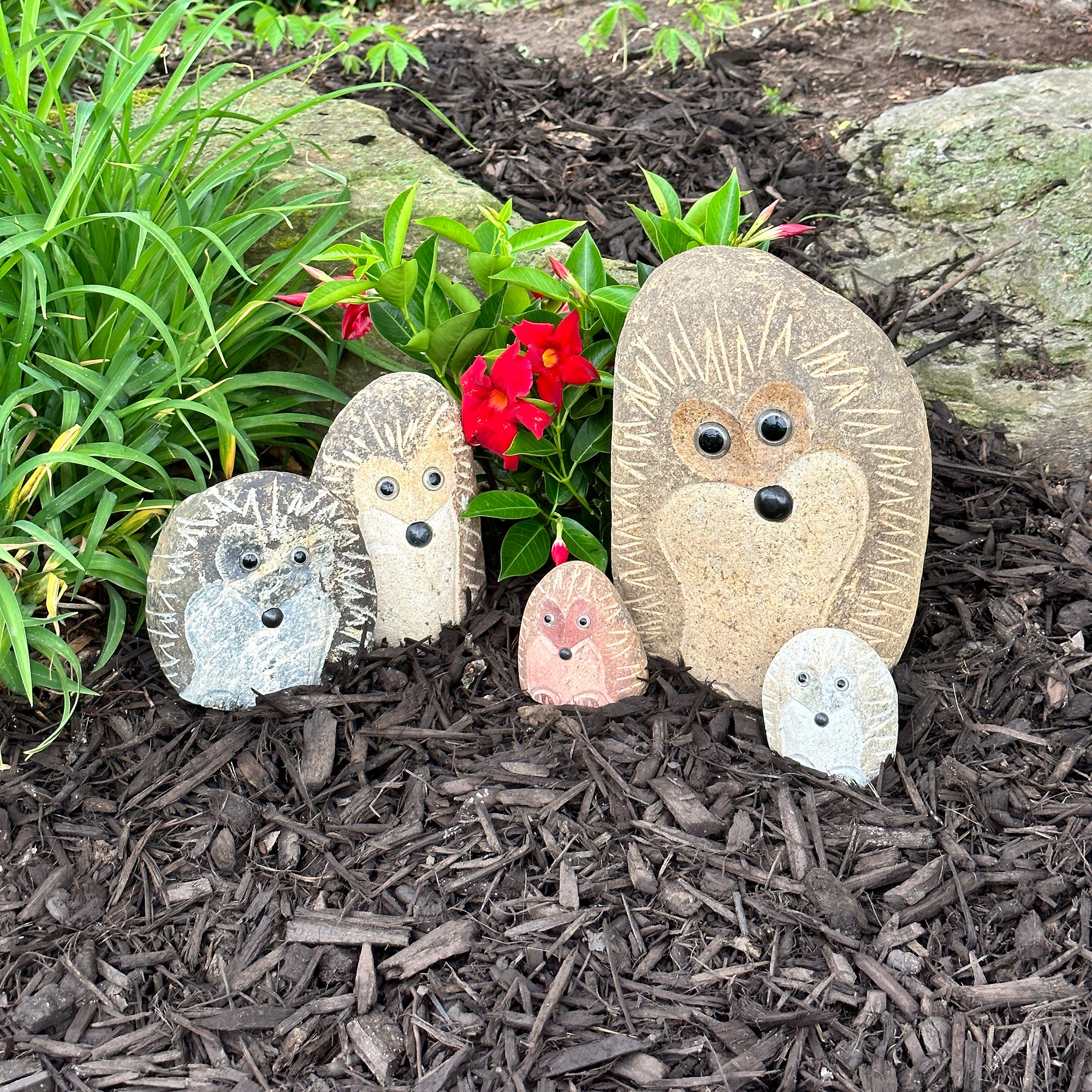 Hand-carved natural granite boulder stone hedgehog family in garden setting.