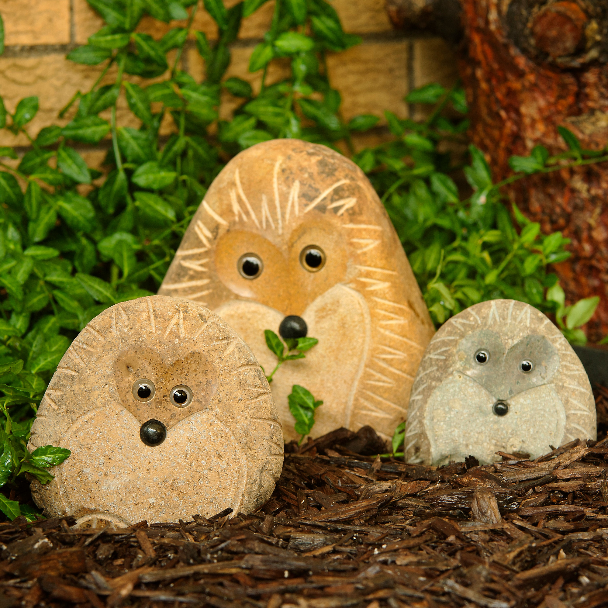 Hand-carved granite stone hedgehogs set of three in a garden setting.