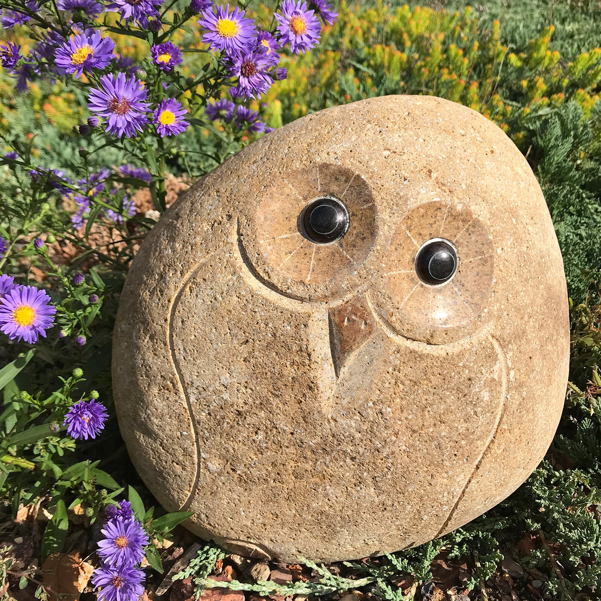 Hand carved natural granite 12&quot; boulder stone owl statue amidst garden flowers.