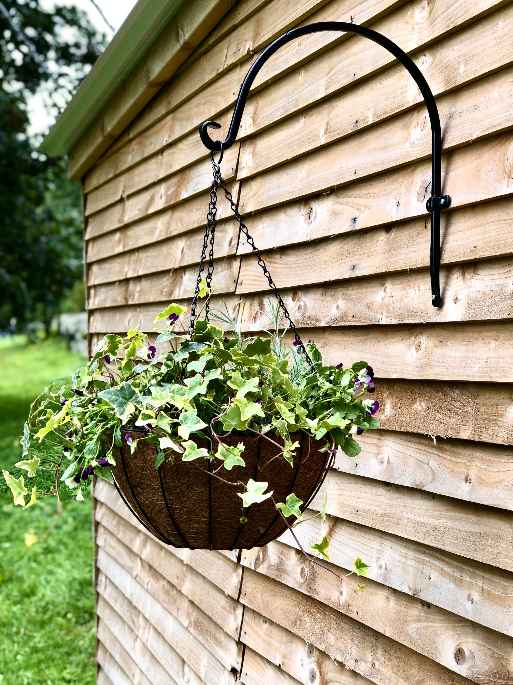 Multipurpose outdoor metal wall hook with hanging basket on wooden wall.