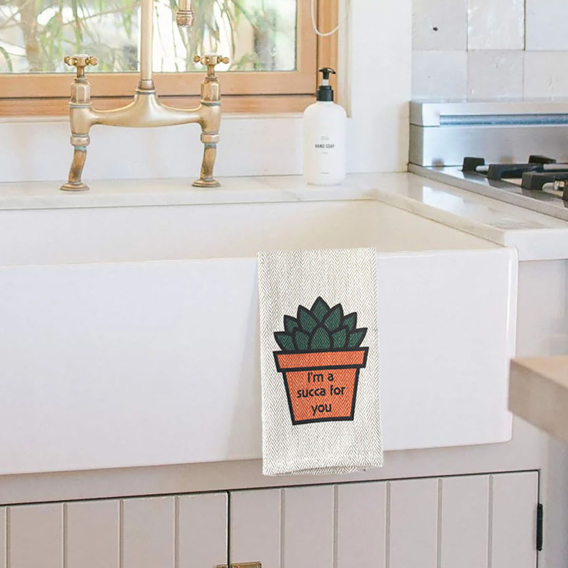 Khaki cotton kitchen tea towel with &quot;I&#39;m a Succa for You&quot; design hanging by a sink.