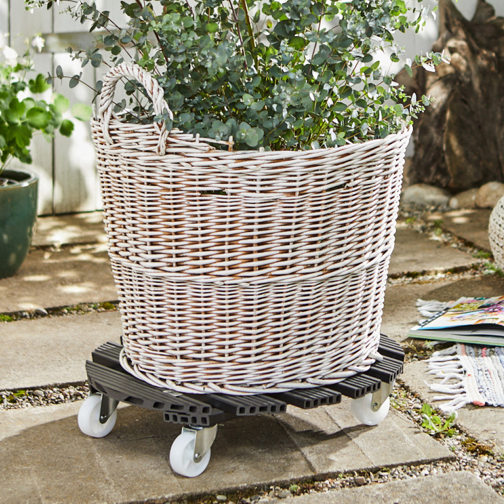 20&quot; gray round WPC plant caddy with brakes in an outdoor setting, supporting a wicker basket planter.