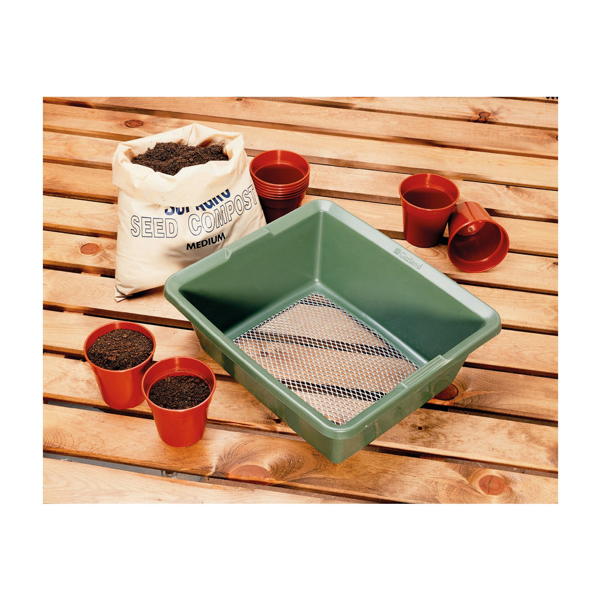 Fine mesh garden sieve for soil and compost sifting on potting table with pots and compost bag.