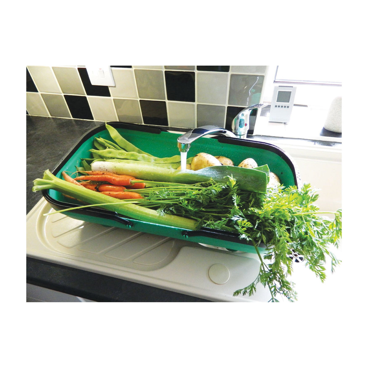 Green colander garden trug with integrated drainage, filled with fresh vegetables, sitting by a sink.