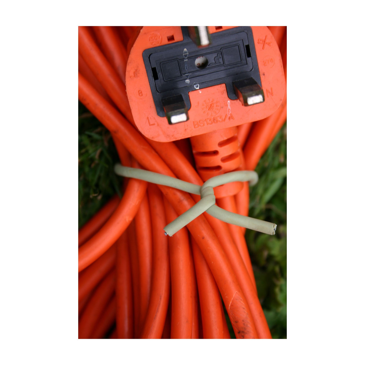 Slim green soft tie wrapped around orange extension cord for plant protection.