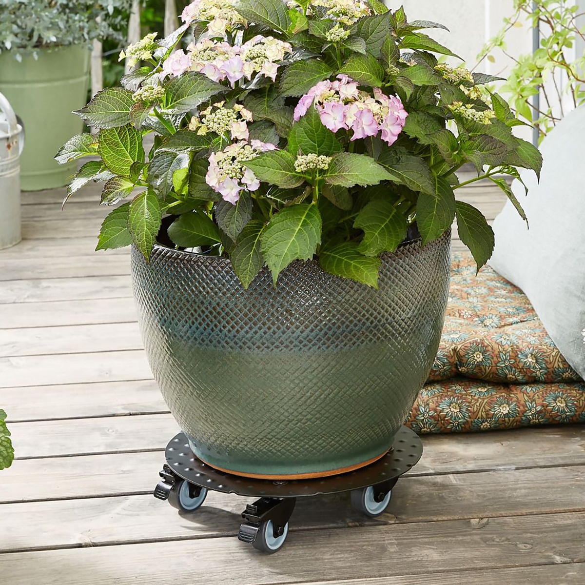 Black aluminum plant caddy with casters and brakes holding a flower pot on a wooden deck.