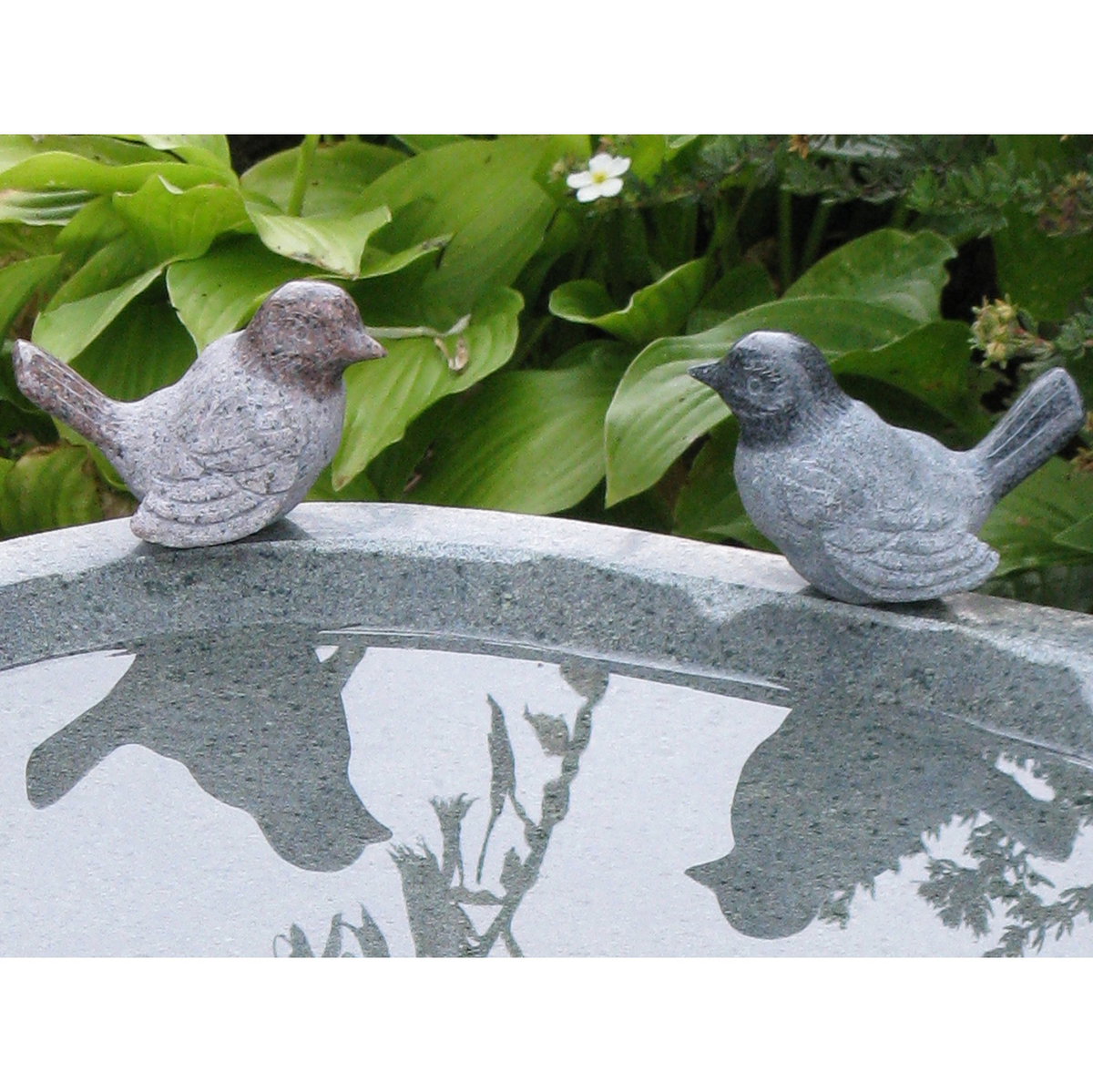 Hand-carved natural granite stone bird in assorted colors on a bird bath.