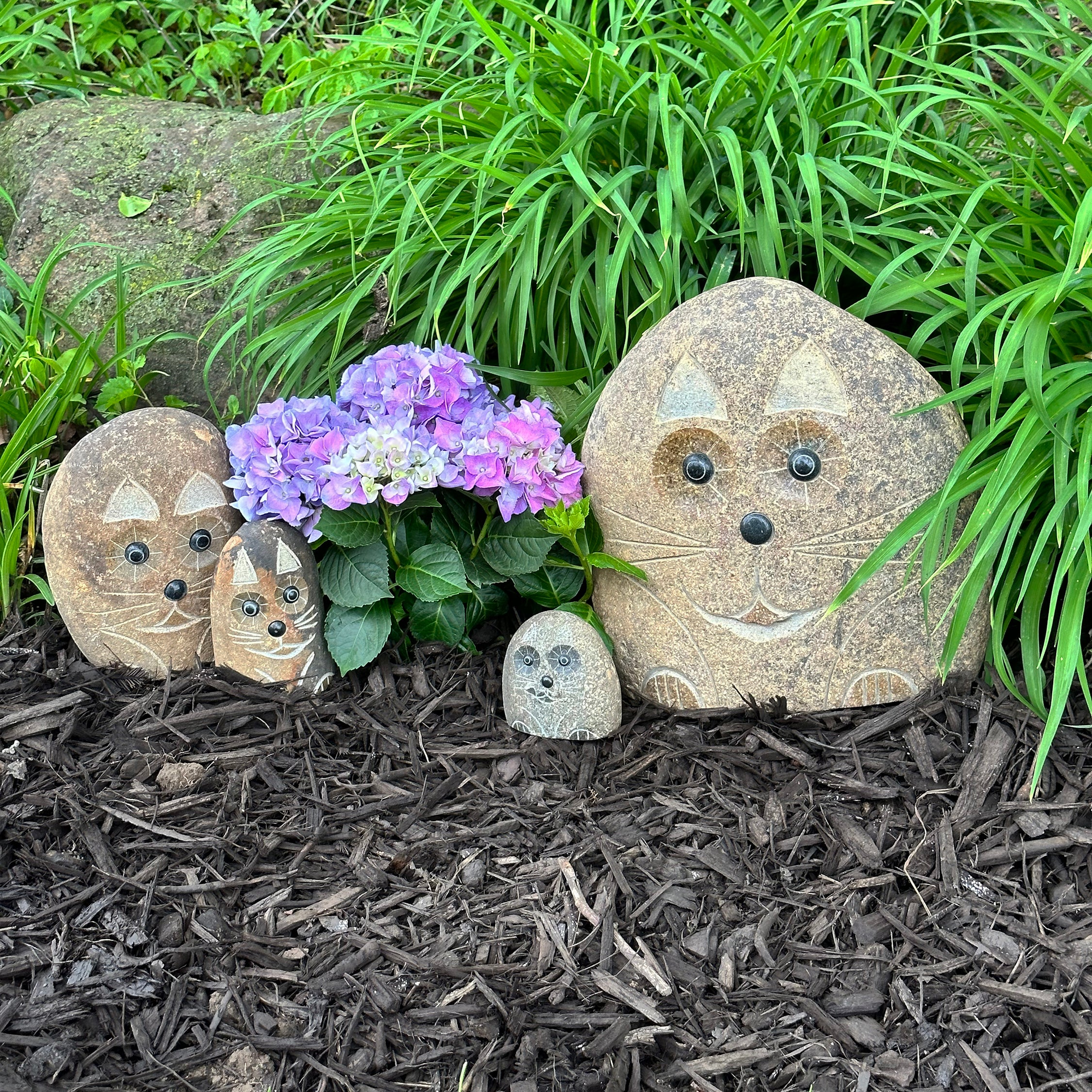 Hand-carved granite boulder stone cat sculptures in garden setting.