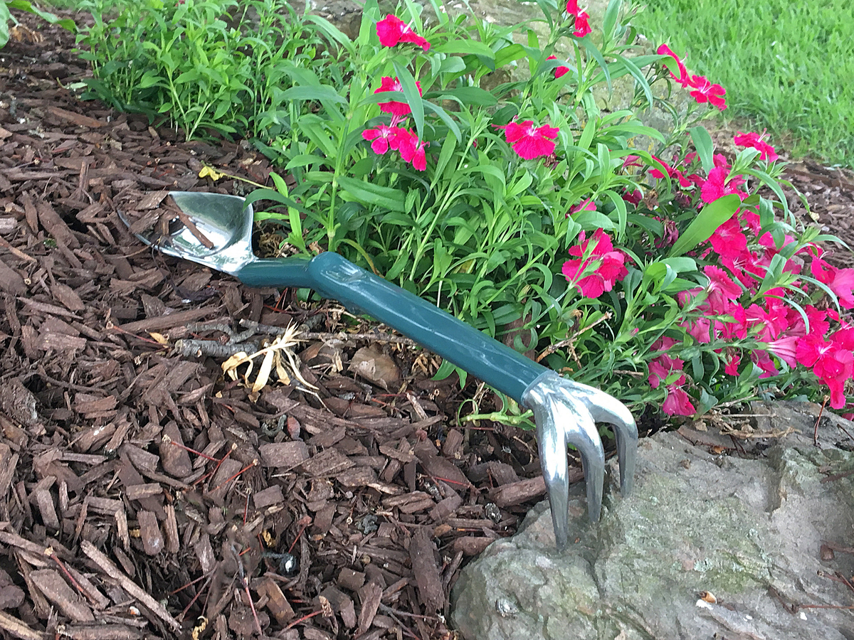 Gardening Trake tool on mulch with pink flowers.