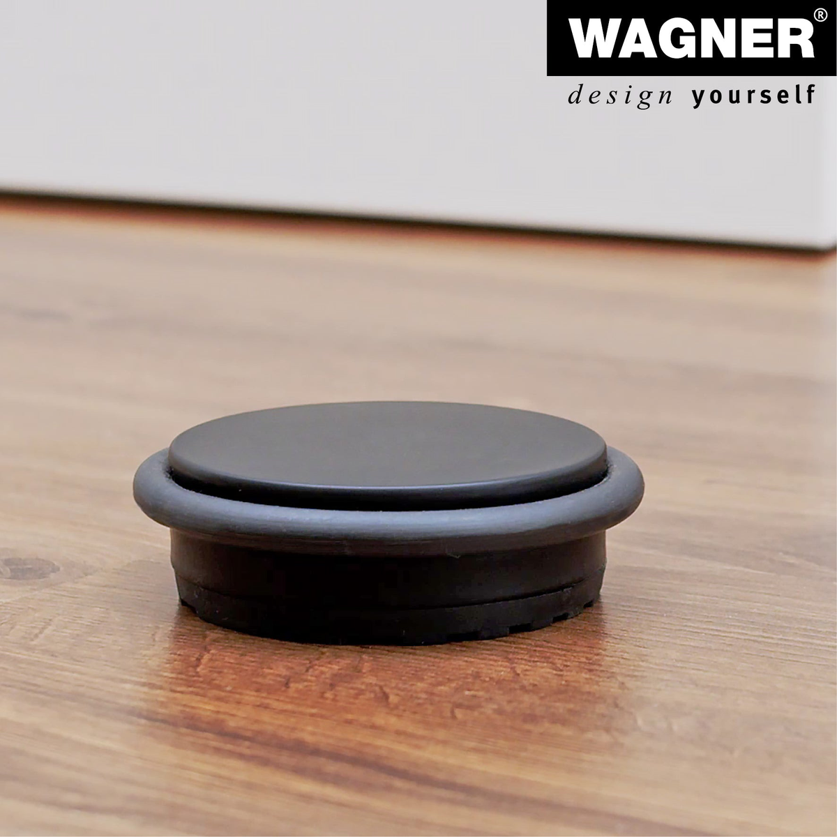 Black door stopper by WAGNER on hardwood floor, 3.86&quot; x 3.86&quot; x 1.18&quot;, industrial steel, rubber cushioning.